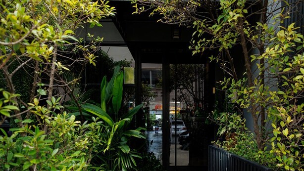 A pathway leading to a building with a glass door, surrounded by lush greenery. - Heyyyy Bangkok - Hostel (Bangkok)