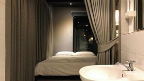 A modern bathroom with a large bed, a sink, and curtains. - Heyyyy Bangkok - Hostel (Bangkok)