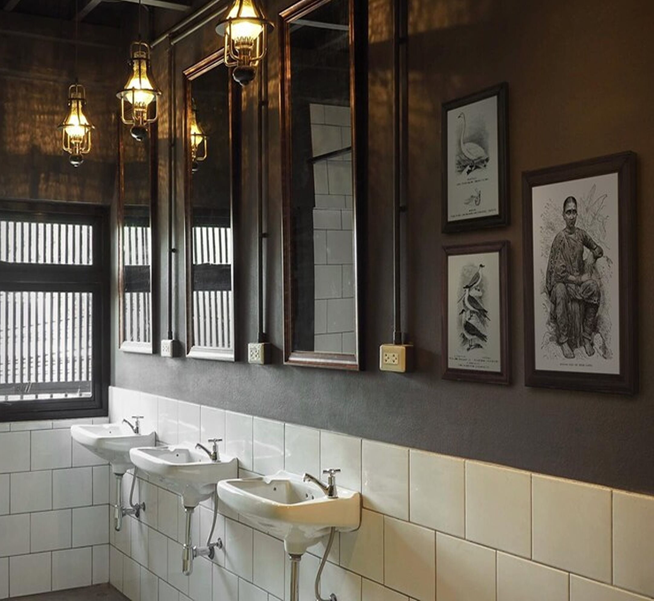 A modern bathroom with three sinks, a large mirror, and framed artwork on the wall.