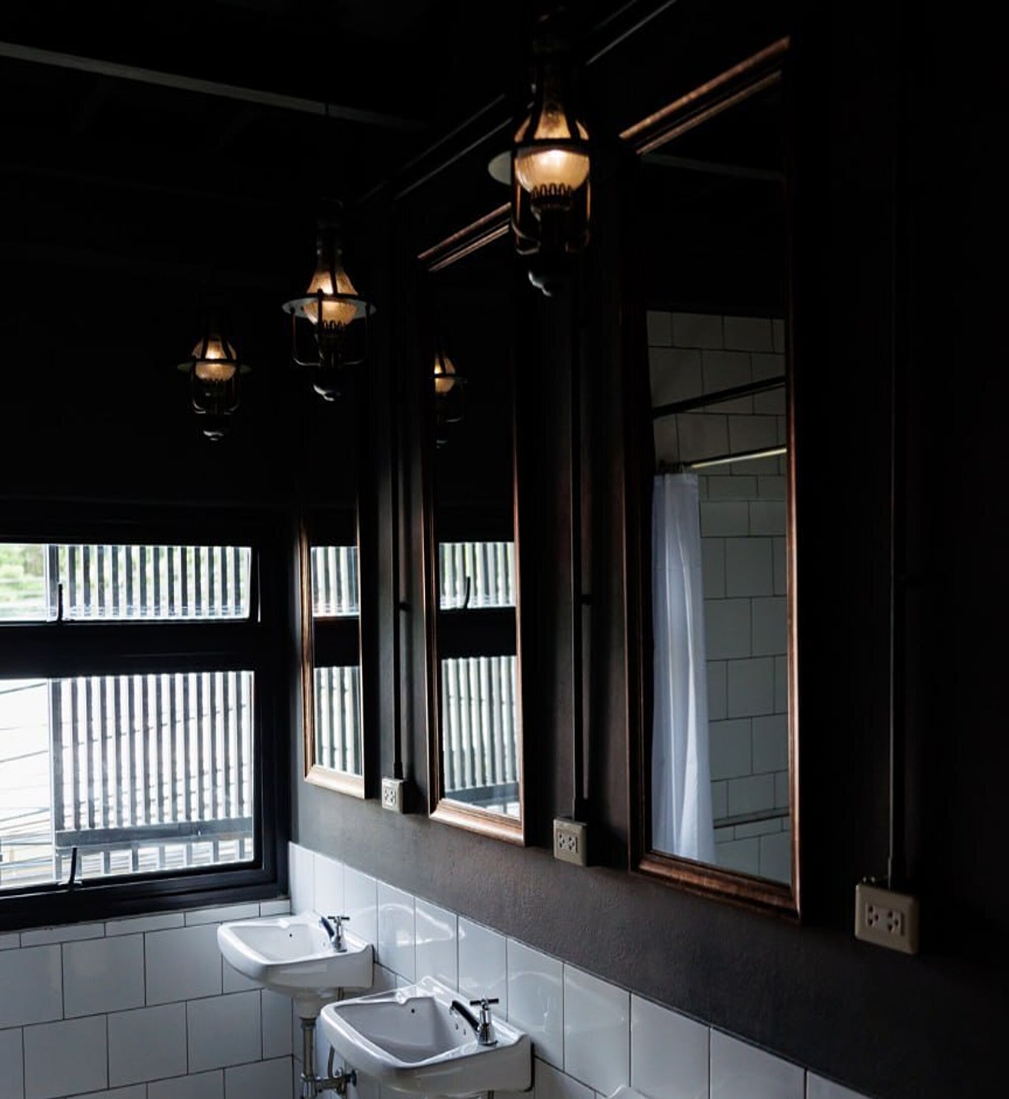 Une salle de bain moderne avec deux vasques, un miroir et trois lampes suspendues.