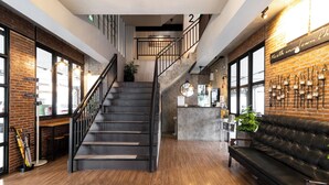 A modern interior with a staircase, wooden flooring, a leather sofa, and a brick wall with a sign. - North Inn Town (Chiang Mai)