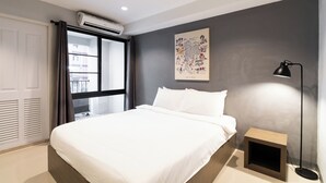 A bedroom with a bed, a window with curtains, an air conditioner, a wall-mounted artwork, and a bedside lamp. - North Inn Town (Chiang Mai)