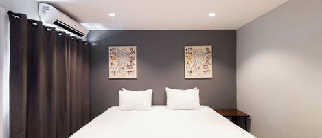 A hotel room with a large bed, dark curtains, two wall-mounted artworks, and a small bedside table.