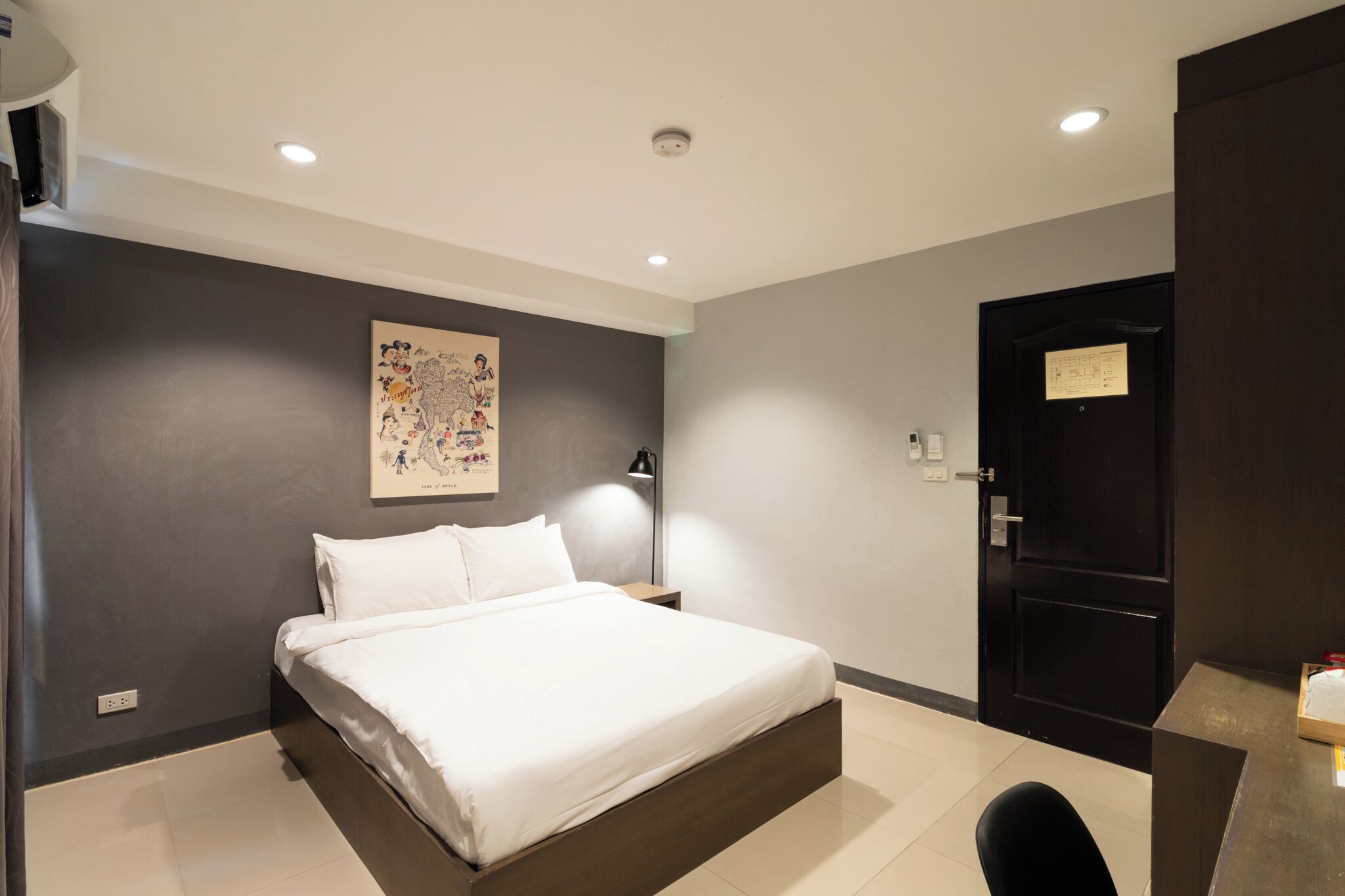 A modern hotel room with a large bed, a nightstand, a desk, and a door with a sign.