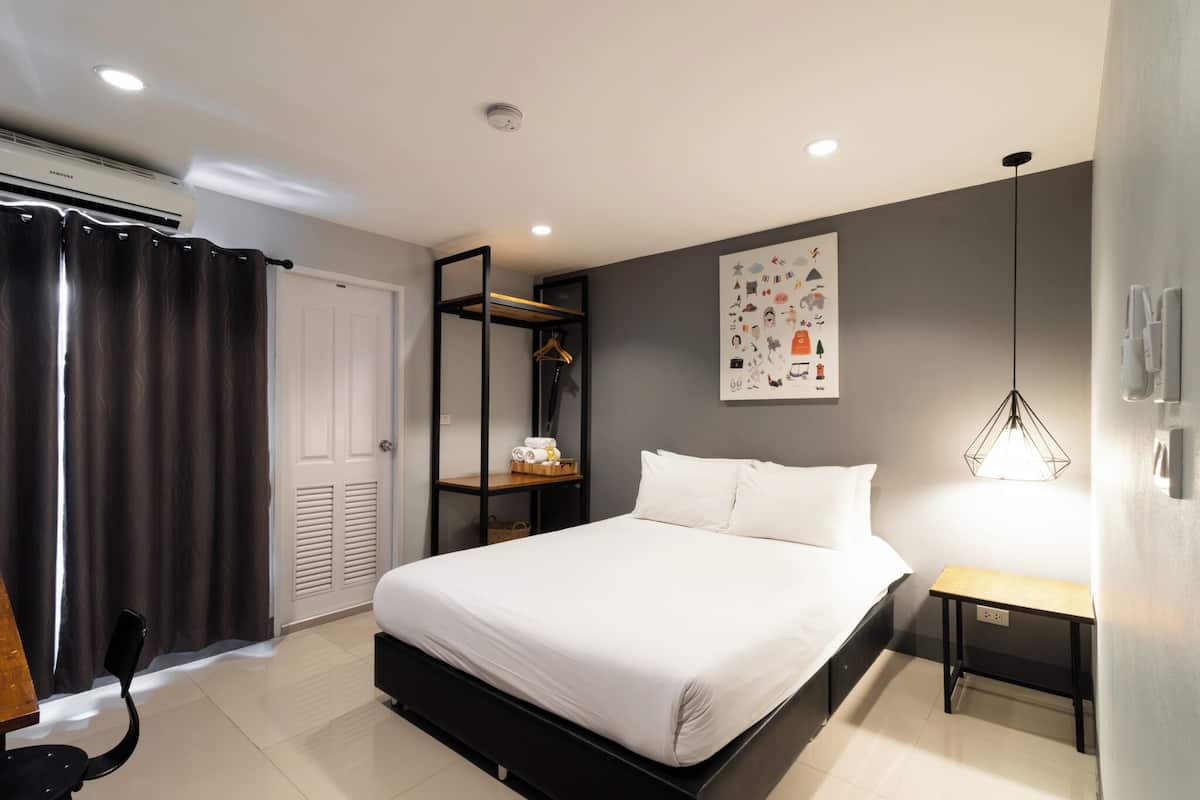 Une chambre moderne avec un grand lit, une table de chevet, une étagère murale avec des serviettes, une porte et un luminaire au plafond.