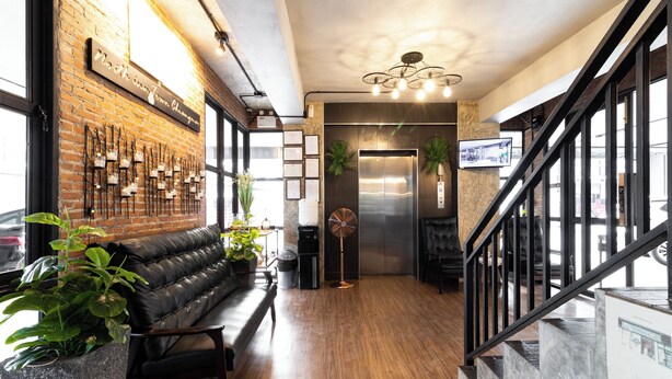 A modern interior with a brick wall, a black leather bench, a fan, and a staircase. - North Inn Town (Chiang Mai)