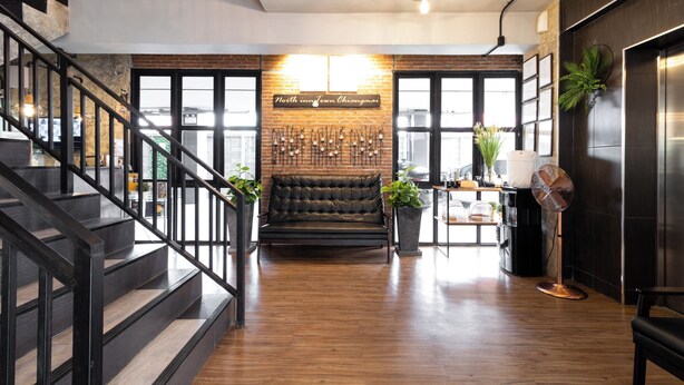 A modern interior with a staircase, a leather sofa, a wall-mounted light fixture, and a sign reading "North in Town Chiangmai". - North Inn Town (Chiang Mai)