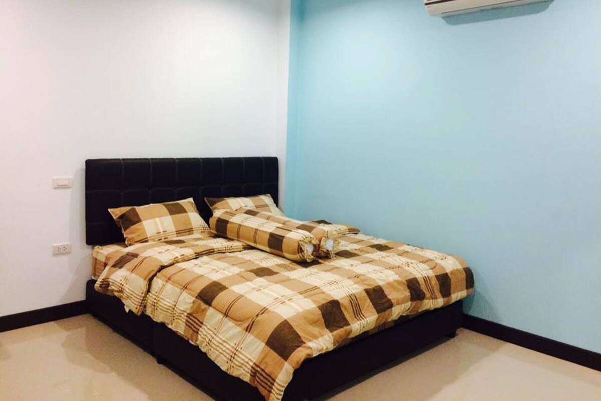 Ein Schlafzimmer mit einem Bett, einem schwarzen Kopfteil, einer blauen Wand und einer Klimaanlage.