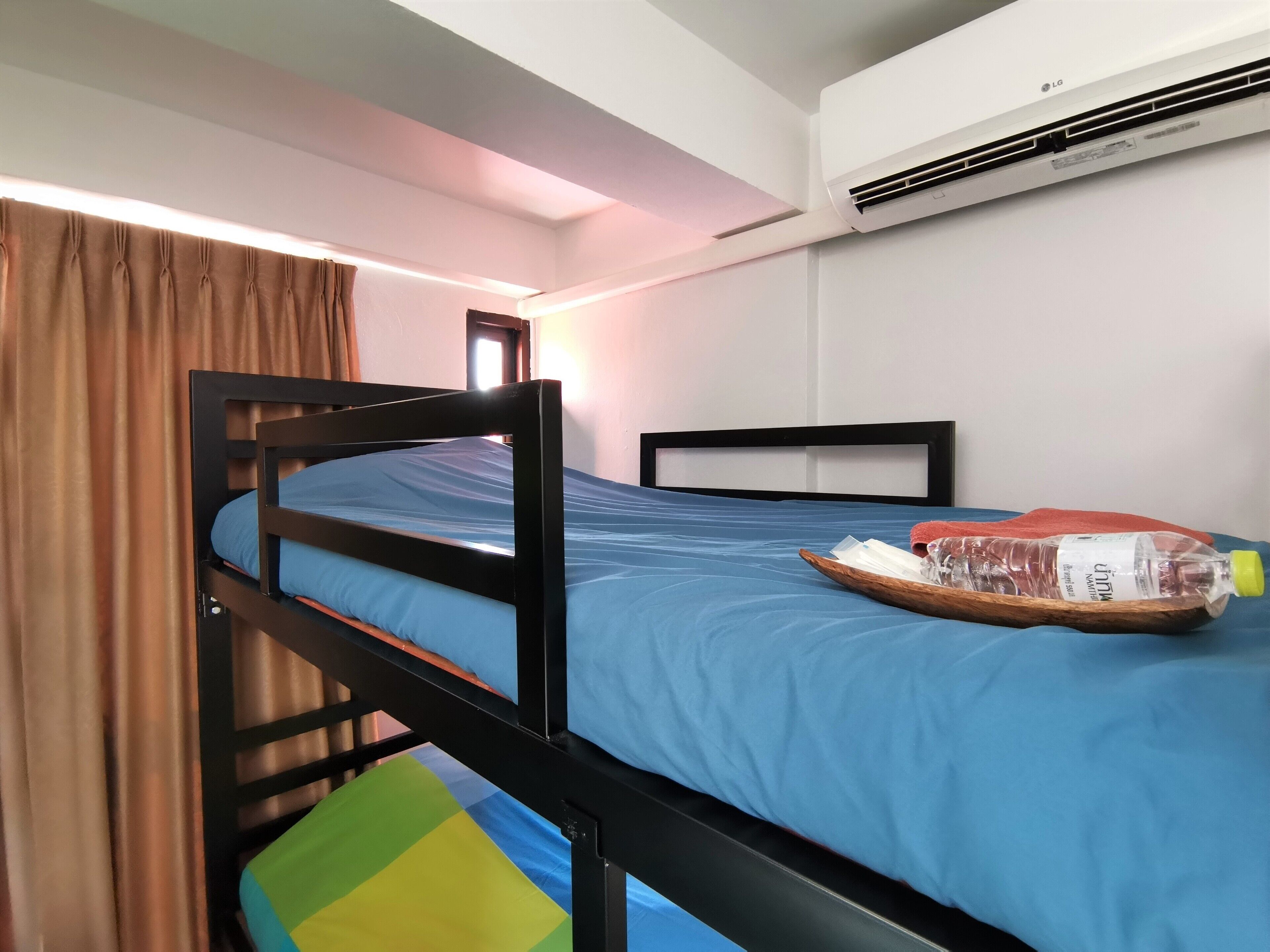 A single bed with a blue mattress, a wooden headboard, and a wooden side table with a bottle and tissues.