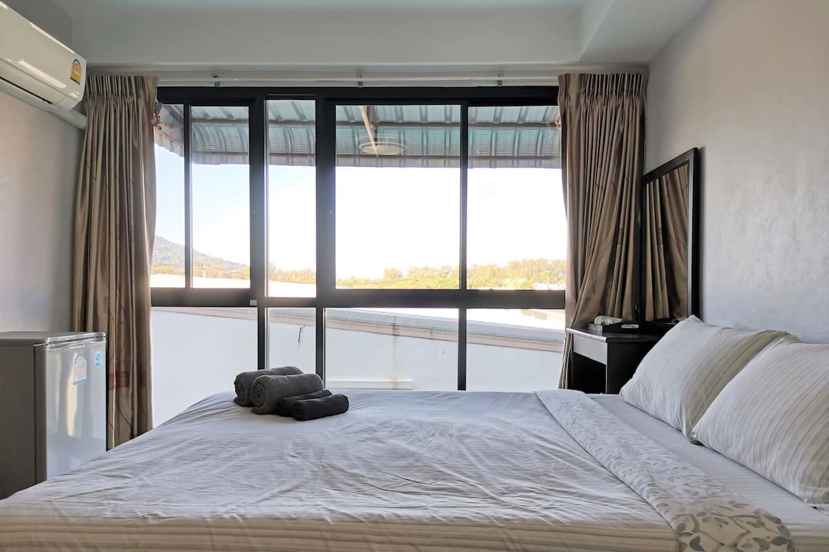 A hotel room with a large bed, a bedside table, a mirror, and a view of a body of water through large windows.