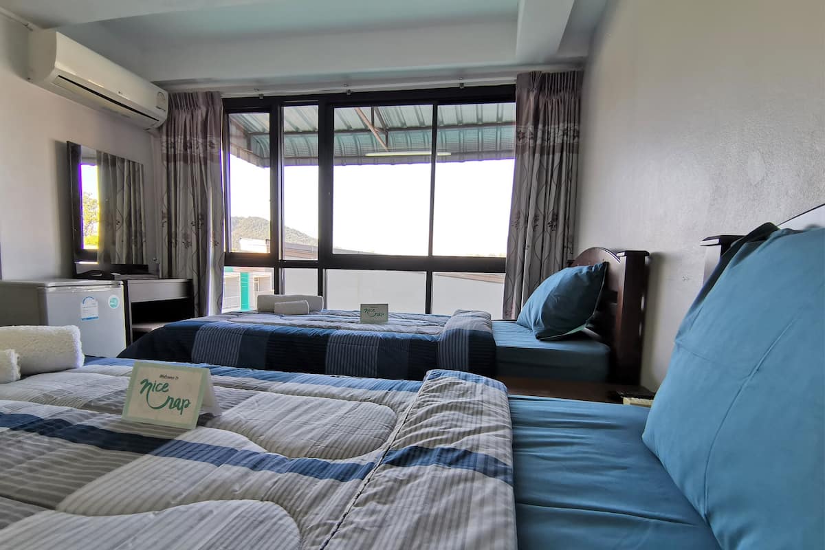 A hotel room with two beds, a desk, an air conditioner, and a view of the outside.