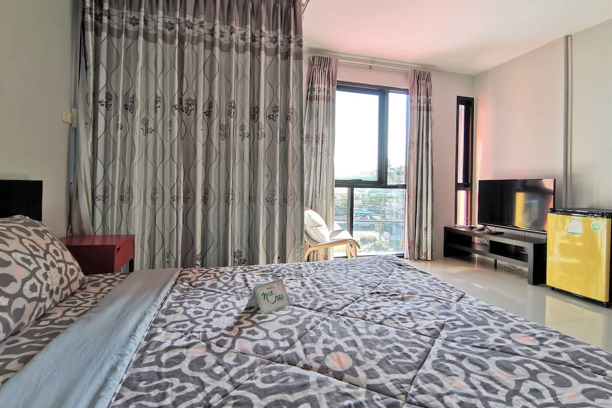 A bedroom with a large bed, a TV, a yellow refrigerator, and a window with curtains.