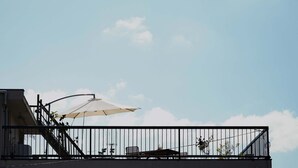 A balcony with a metal railing, a white umbrella, and a clear blue sky.