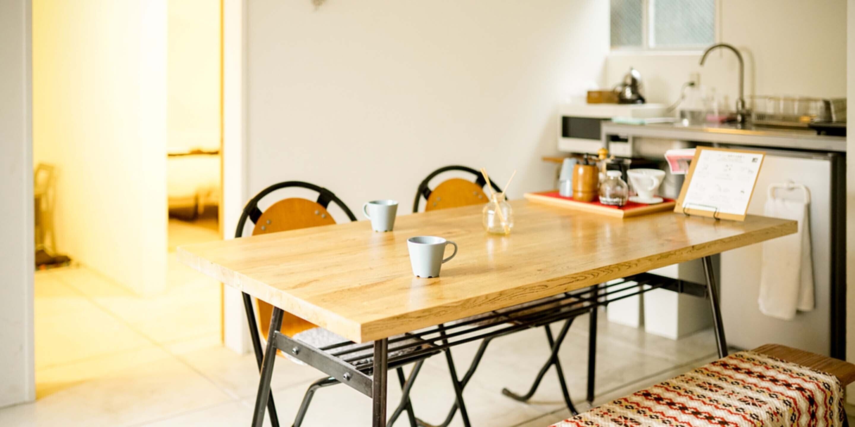 A dining area with a wooden table, four chairs, a bench, and a kitchen in the background.