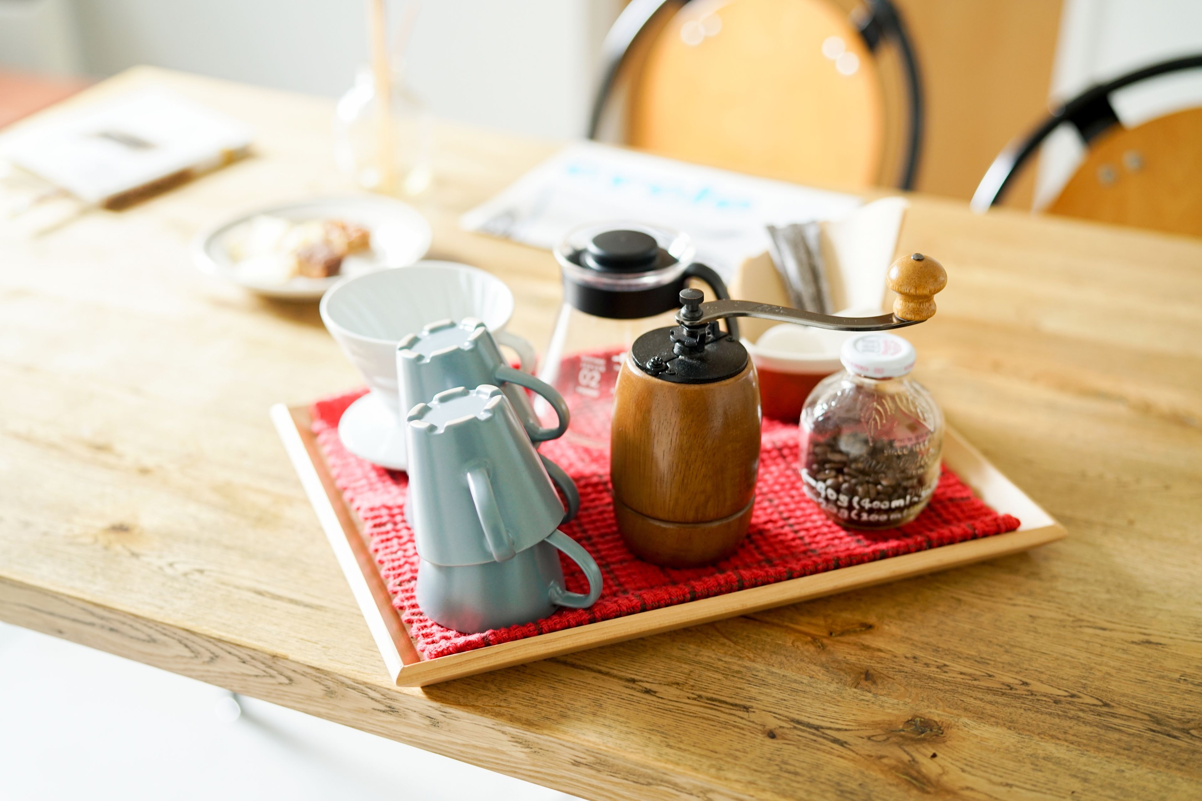 Una mesa de madera con una bandeja que contiene una cafetera, una taza, un azucarero y un frasco pequeño.