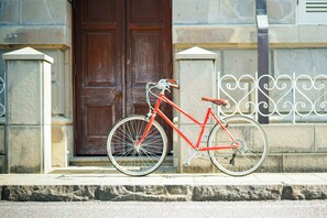 A red bicycle parked in front of a building with a large wooden door and decorative metal railings. - Route - Hostel (Nagasaki)