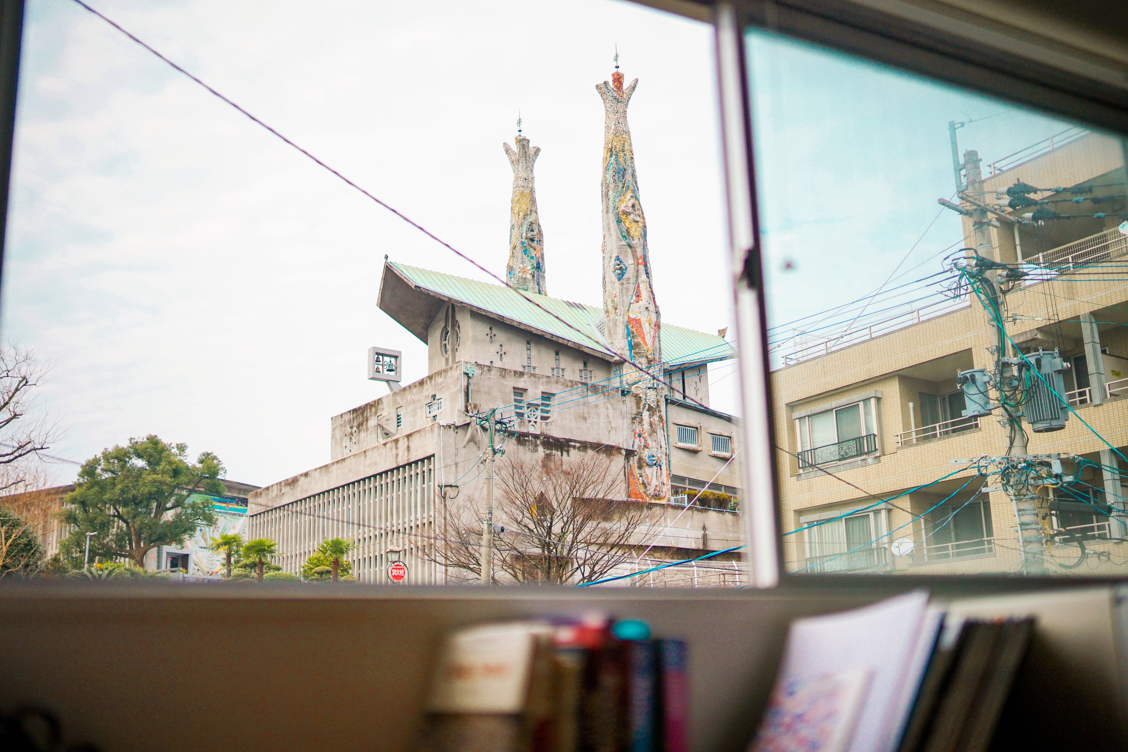 A view of a building with two tall towers, a window with a view of the building, and some books on a table.
