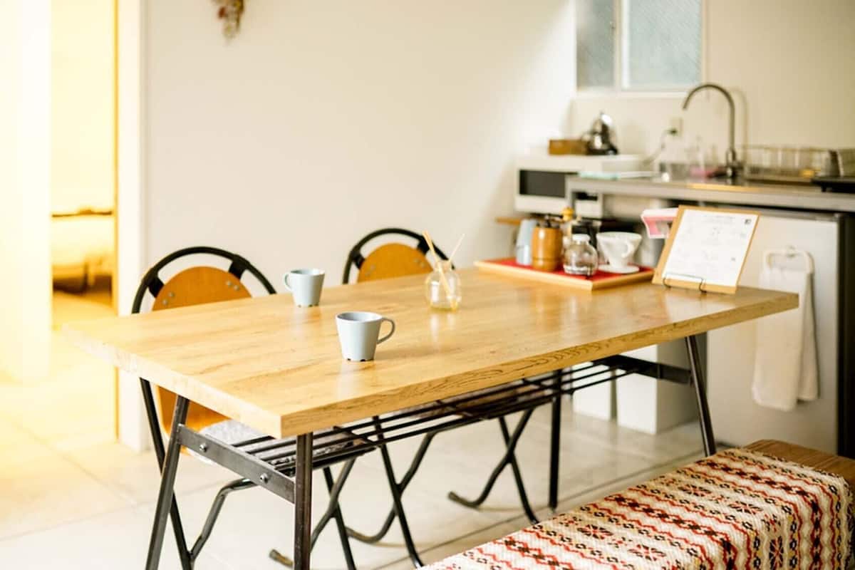 A dining area with a wooden table, four chairs, a bench, and a kitchen in the background.