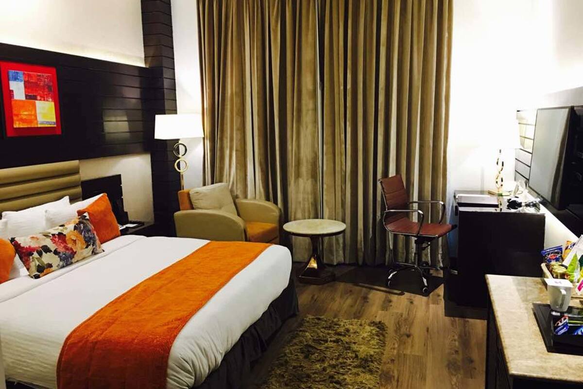 Ein Hotelzimmer mit einem großen Bett, einem Schreibtisch, einem Sessel, einem kleinen Tisch und einem Fernseher.