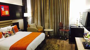 Ein Hotelzimmer mit einem großen Bett, einem Schreibtisch, einem Sessel, einem kleinen Tisch und einem Fernseher.