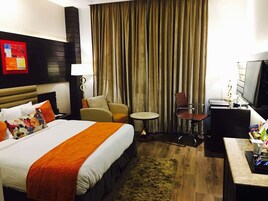 Ein Hotelzimmer mit einem großen Bett, einem Schreibtisch, einem Sessel, einem kleinen Tisch und einem Fernseher.