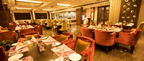 A spacious dining area with multiple tables set for guests, featuring plush seating and a modern interior design.