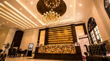 A hotel reception area with a large chandelier, a reception desk, and seating arrangements.