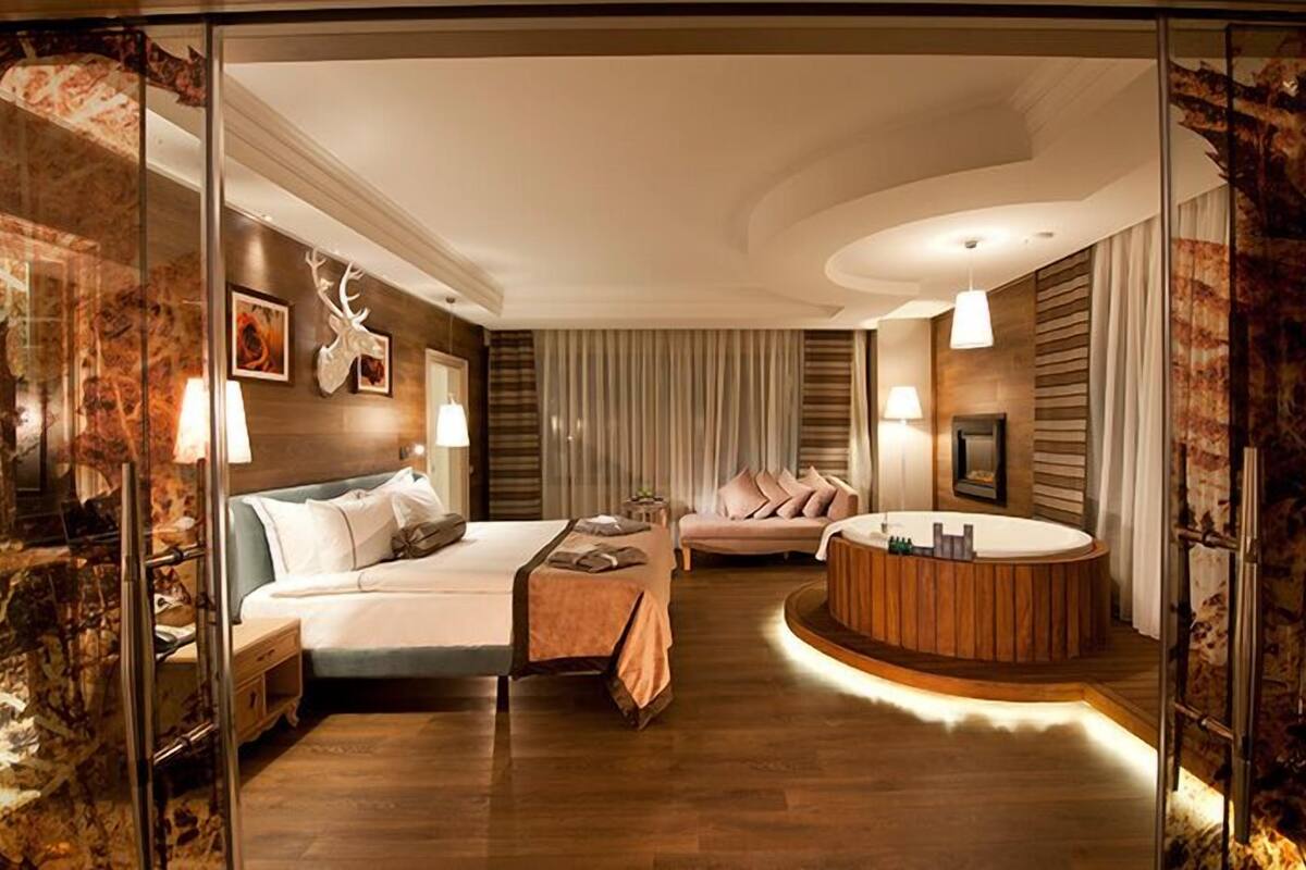 Una habitación de hotel moderna con una cama, un sofá, una zona de estar circular y una chimenea.