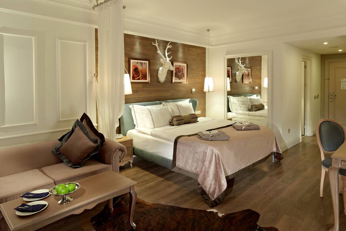 Una habitación de hotel con una cama grande, un rincón de descanso con sofá y mesa, y un escritorio con silla.