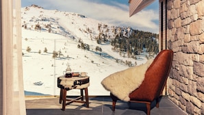 Een gezellige kamer met uitzicht op een besneeid berglandschap, een leren fauteuil en een tafeltje met een kopje en schotel.