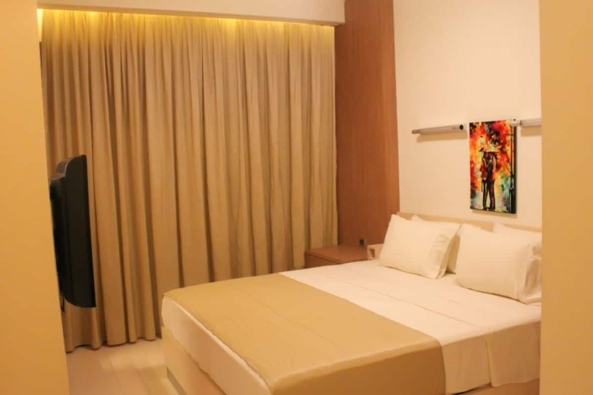 A hotel room with a bed, curtains, a painting on the wall, and a television.