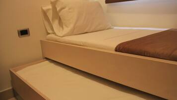 A single bed with a mattress and a pillow, a small bedside table, and a window with blinds.