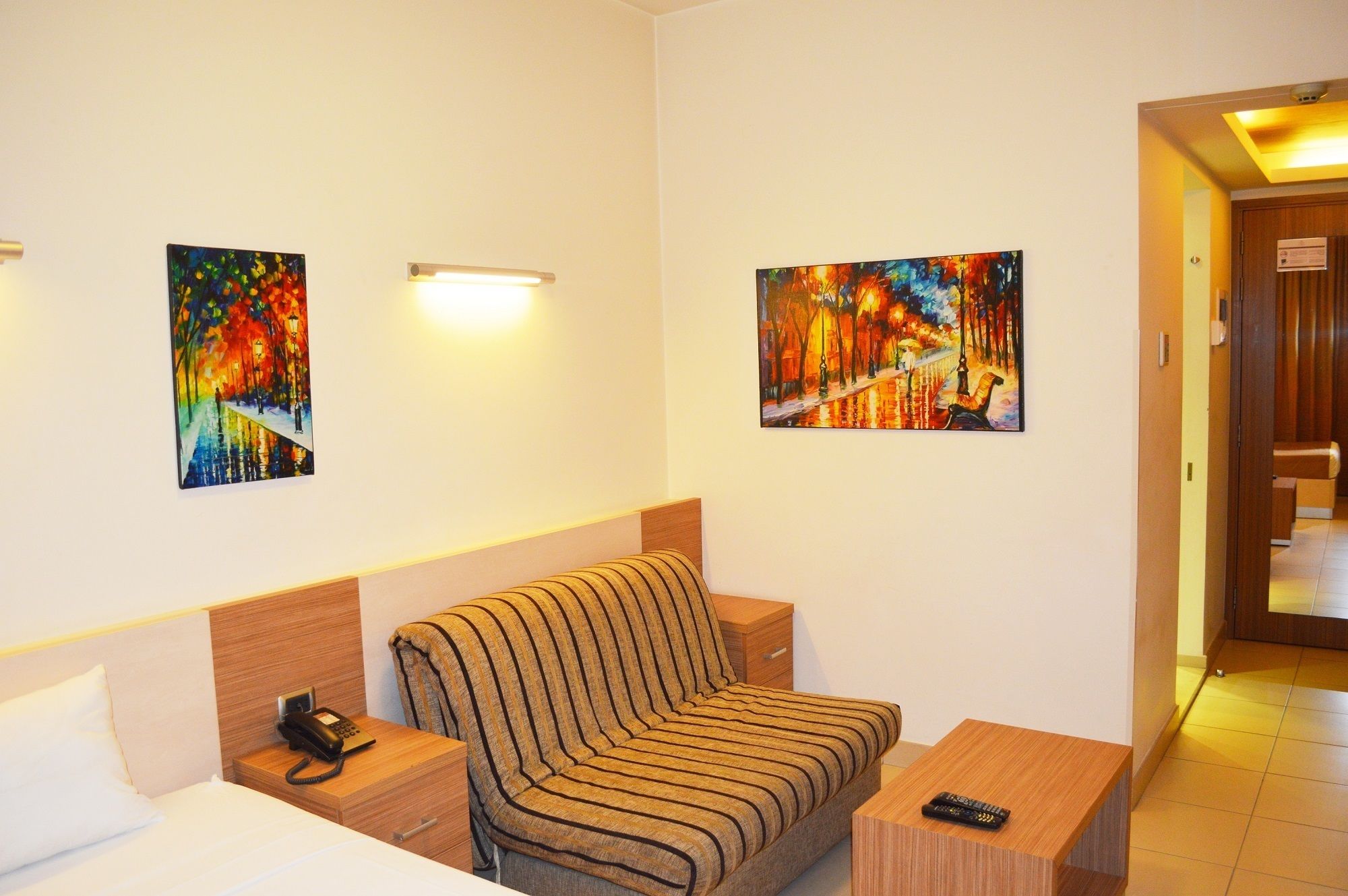 Een hotelkamer met een bed, een gestreept sofa, een nachtkastje met een telefoon, en twee schilderijen aan de muur.