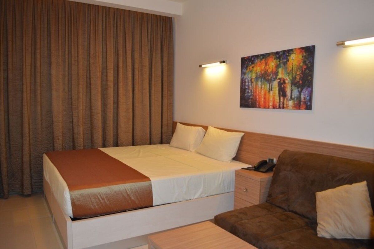 A hotel room with a large bed, a brown sofa, a nightstand with a phone, and a painting on the wall.