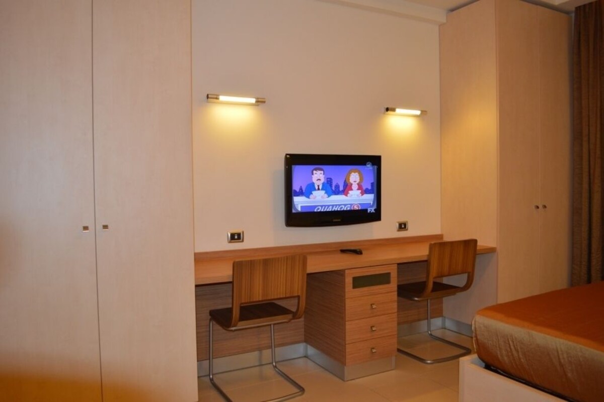 A hotel room with a wooden desk, two chairs, a television, and a bed.