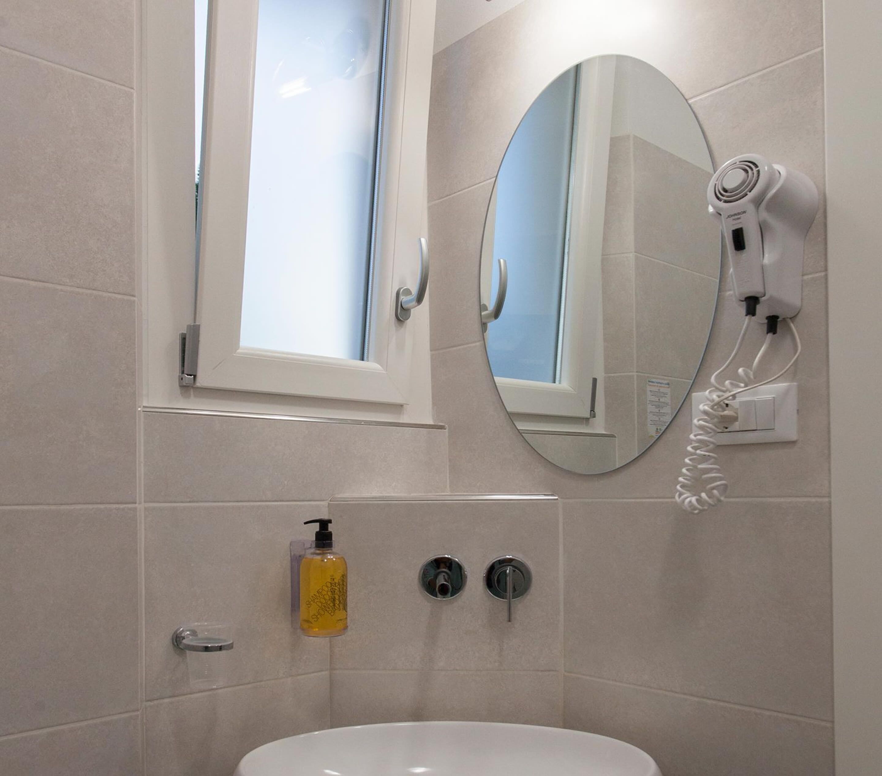 A bathroom with a white sink, a mirror, a hairdryer, and a window.