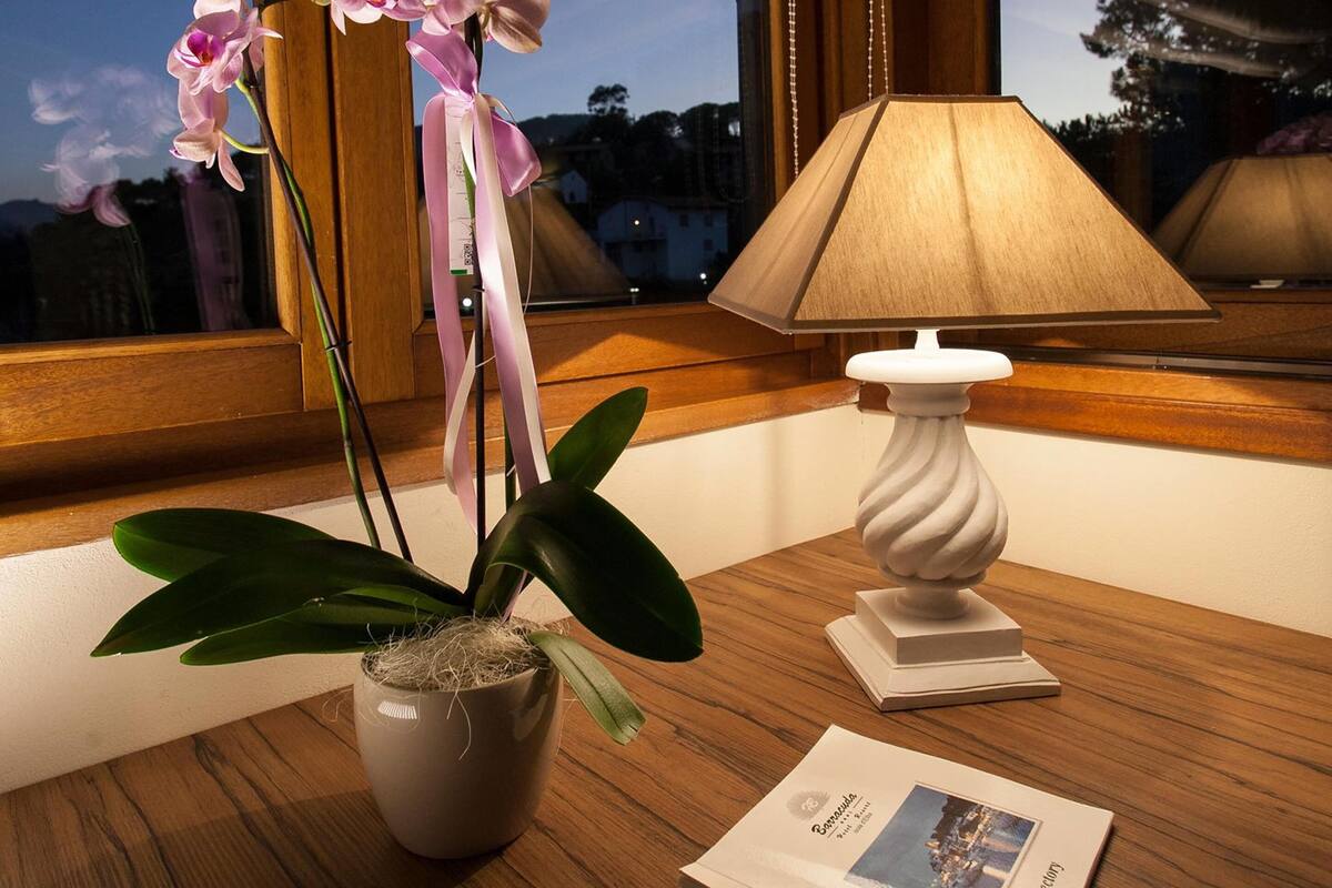 A room with a wooden table, a potted orchid, a lamp, and a framed photo.