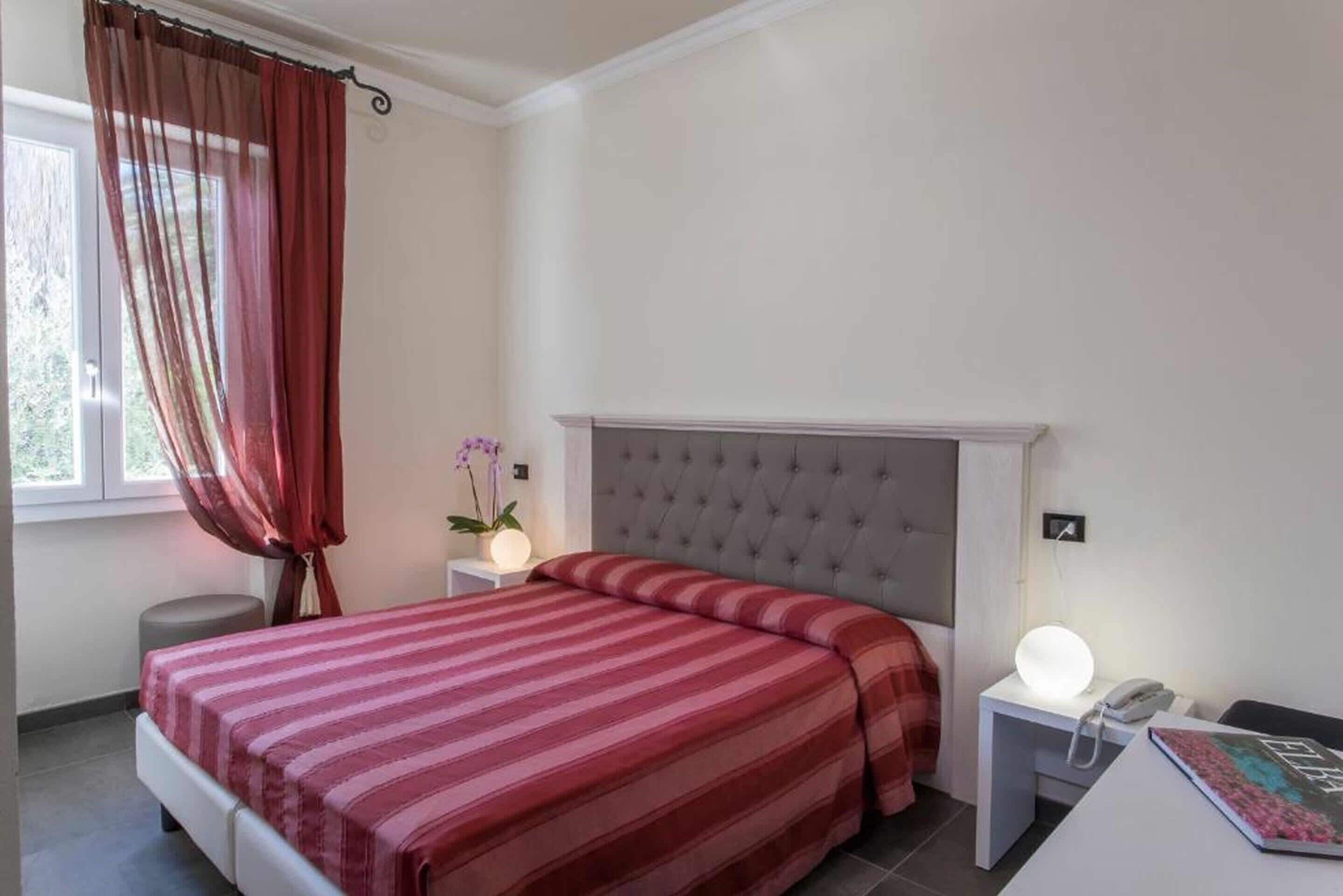 Une chambre à coucher avec un lit, une table de chevet avec une lampe, une commode et une fenêtre avec des rideaux.