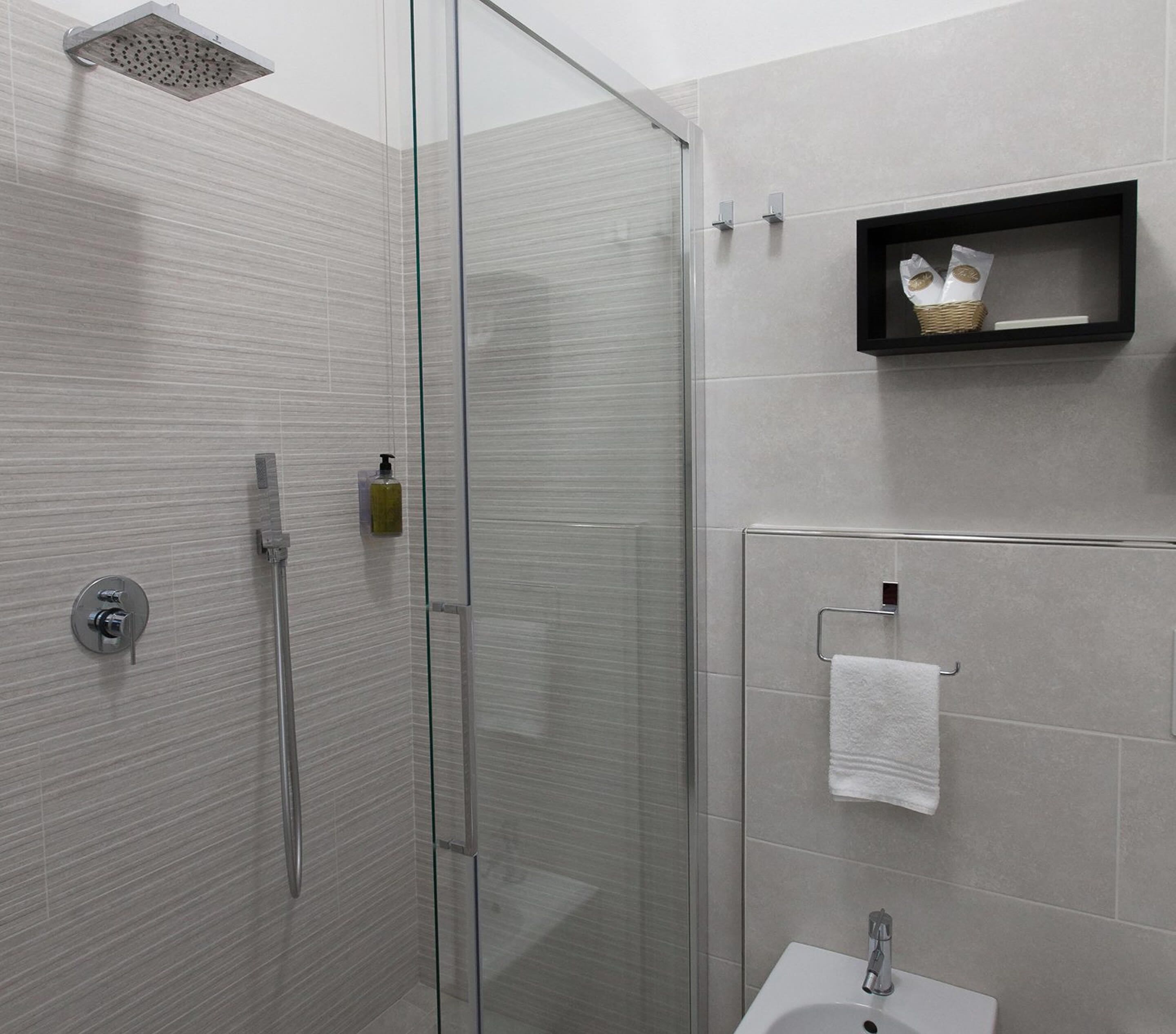A modern bathroom with a glass shower enclosure, a white sink, and a small shelf with a decorative item.