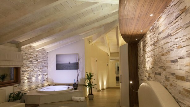 Ein modernes Schlafzimmer mit Steinwand, einem großen Bett, einer Sitzecke und einem Badezimmer mit Badewanne.