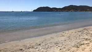 Ein Strand mit klarem Wasser, sandigem Ufer und Hügeln im Hintergrund.