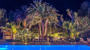 Ein Poolbereich bei Nacht mit Palmen und Liegestühlen.