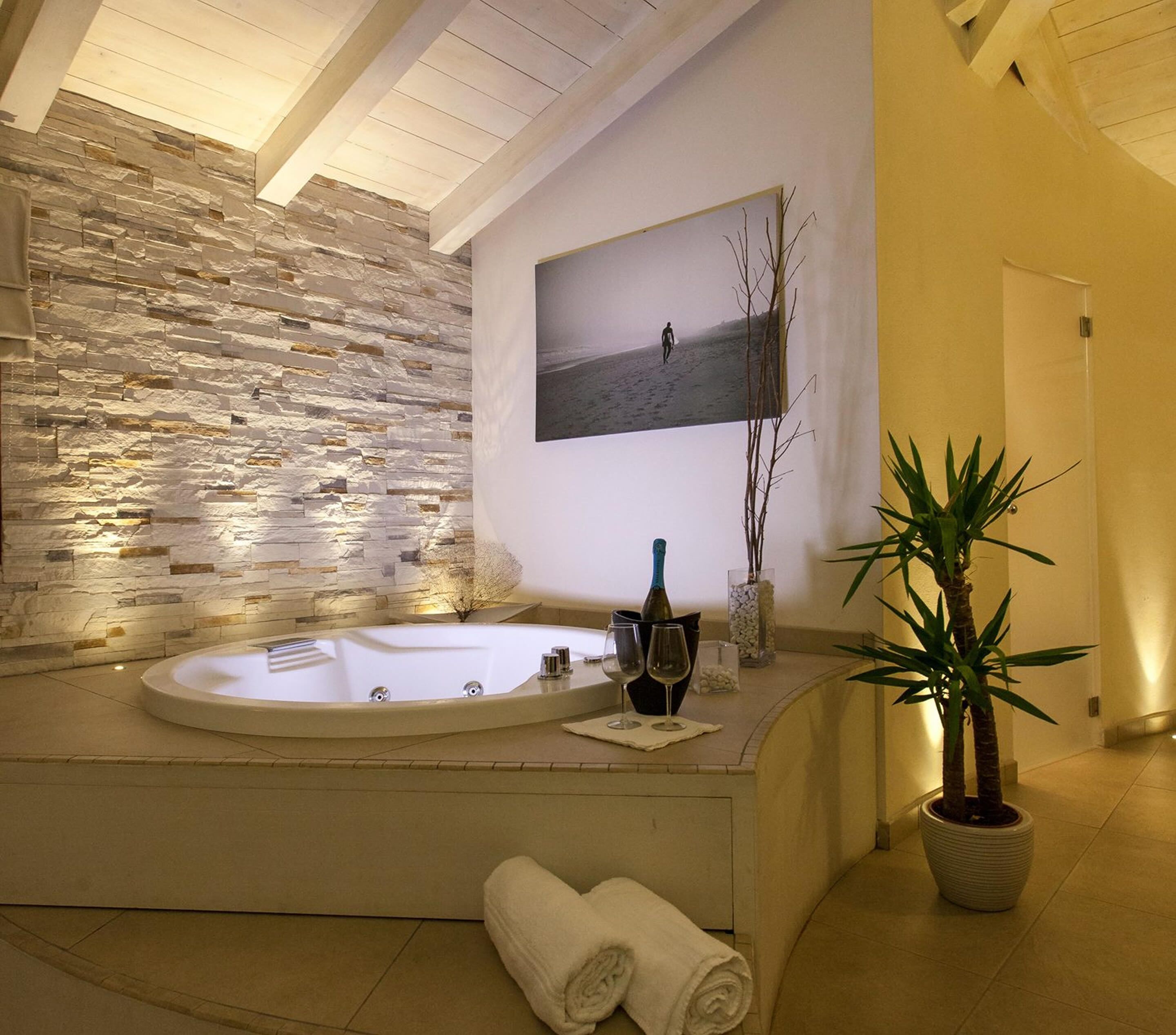 Ein Spa-Badezimmer mit Steinwand, einer großzügigen Badewanne, einem Strandbild und einem Topf mit Pflanze.