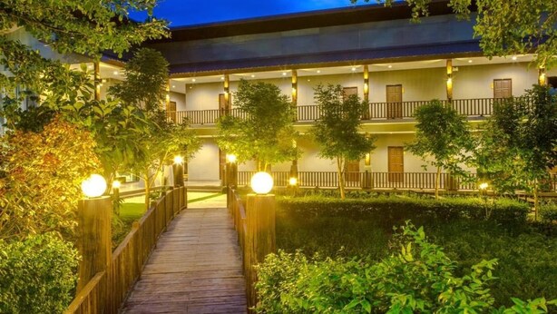 Un hôtel doté d’une terrasse en bois qui mène à un bâtiment comportant de nombreux balcons et un espace piscine.