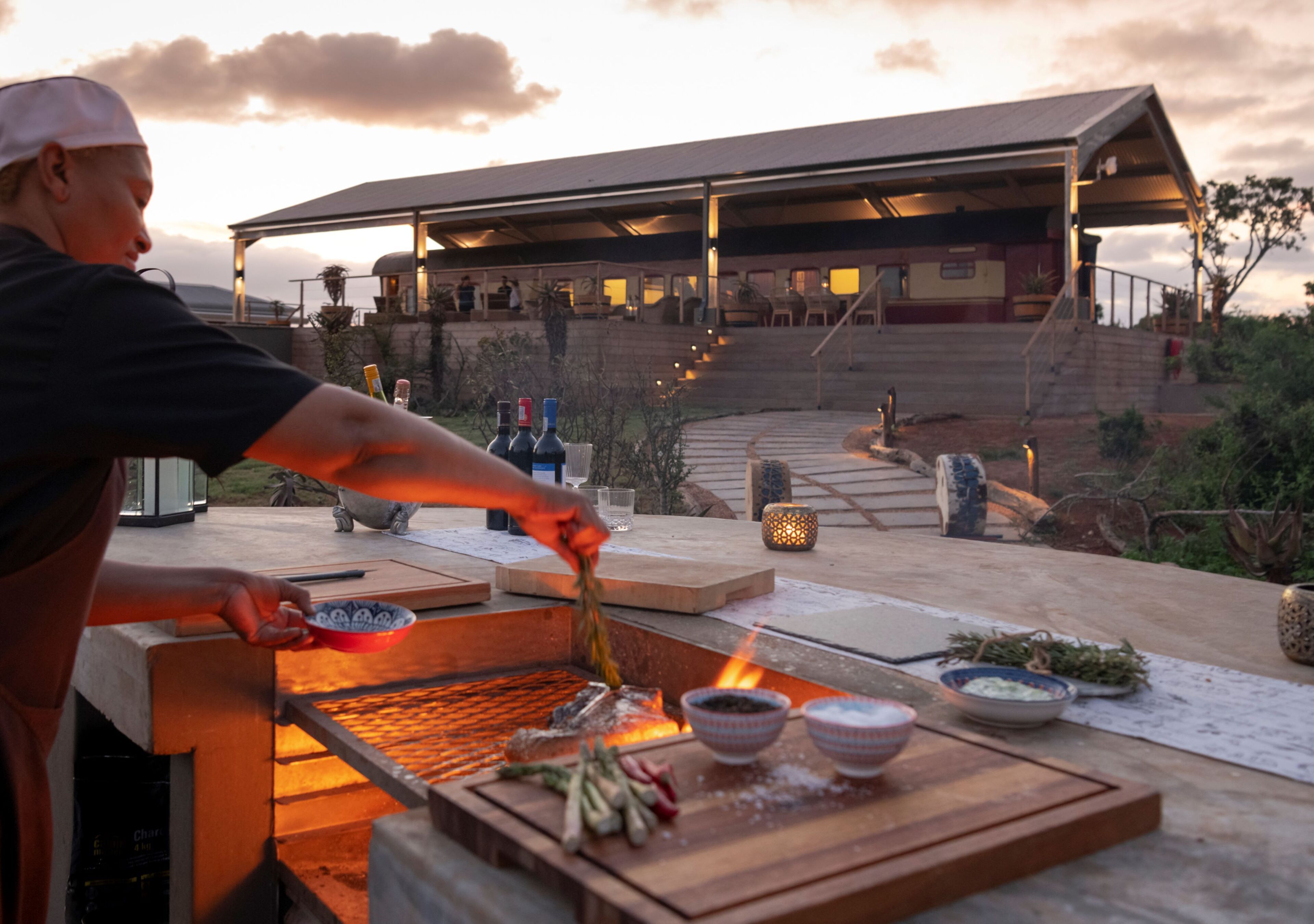 A chef grilling food outdoors with a view of a building in the background.