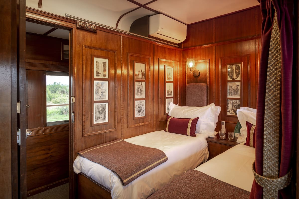 A room with two beds, wooden paneling, framed pictures, a window, and an air conditioning unit.