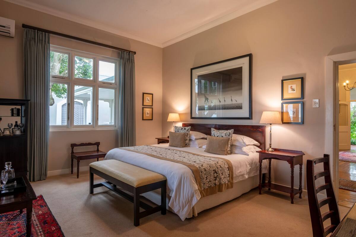 A neatly arranged bedroom with a large bed, bedside tables, a bench, and a window with curtains.