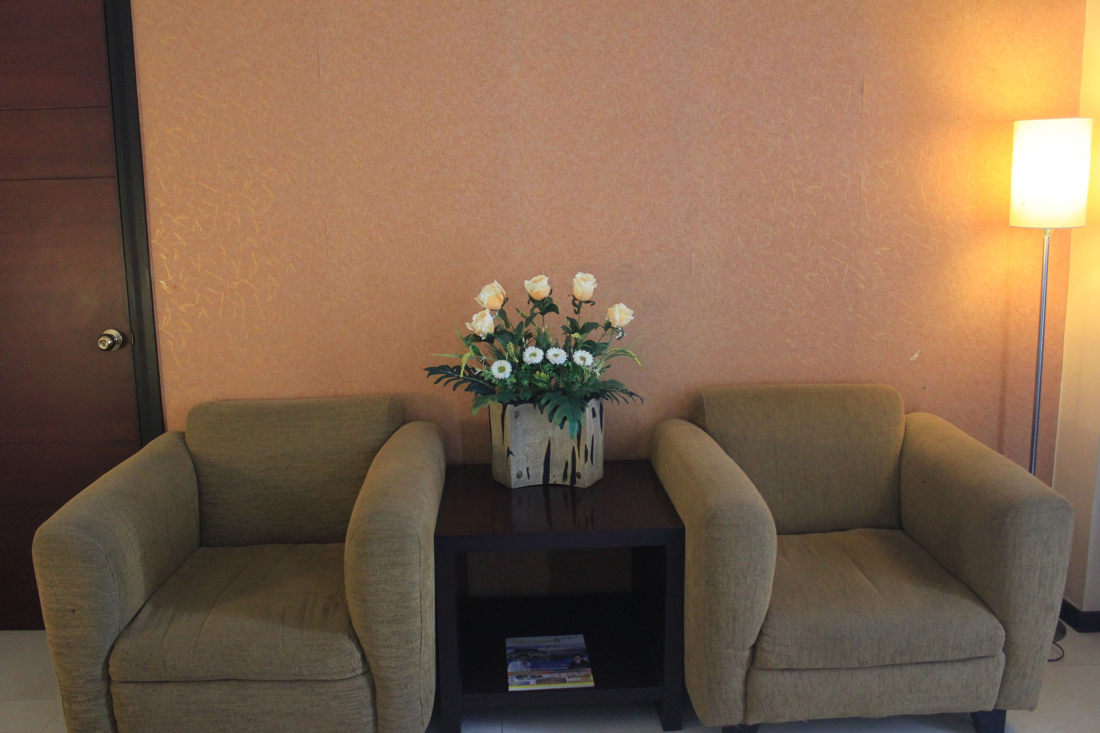 Une pièce comprenant deux fauteuils, une petite table ornée d’un vase de fleurs et une lampe.
