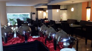 Un restaurante con varias mesas, algunas cubiertas con manteles rojos, y vistas a zonas verdes.