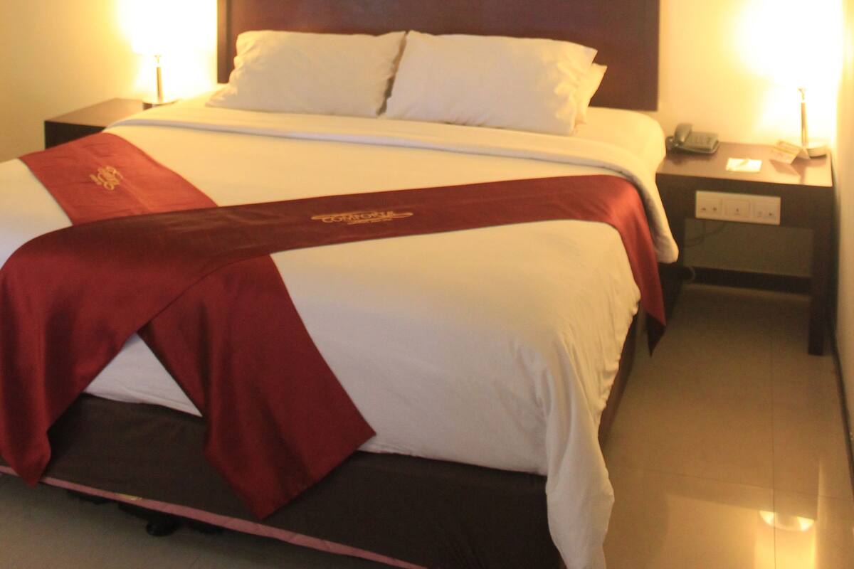 Una habitación de hotel con una cama bien hecha, un cabecero de madera y dos lámparas de noche.